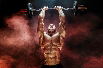 Portrait of muscular man lifting dumbbell in red smoke. Studio shot. Exercise for triceps....