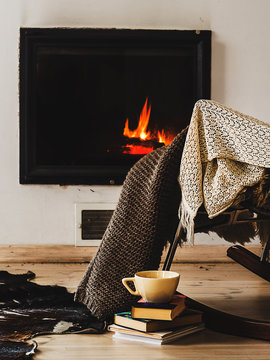 Rocking chair with knit rug, books and cup of tea or coffee before fireplace