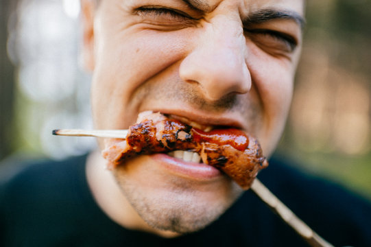 Facial Expression Of Man Eating With Disgust Grilled Sausage Outdoor. Vegetarian Feeling Pain And Suffering Trying Meat. Pork Is Bad. Recycled Dead Animal. Tasteless Fried Food. Adult Male Biting.