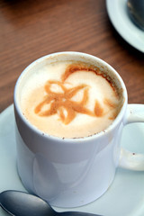 Obraz premium Delicious foamy cappuccino on a white cup on a plate.