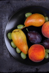 Pears, peaches, grapes and plums on a black plate in retro style on a dark background