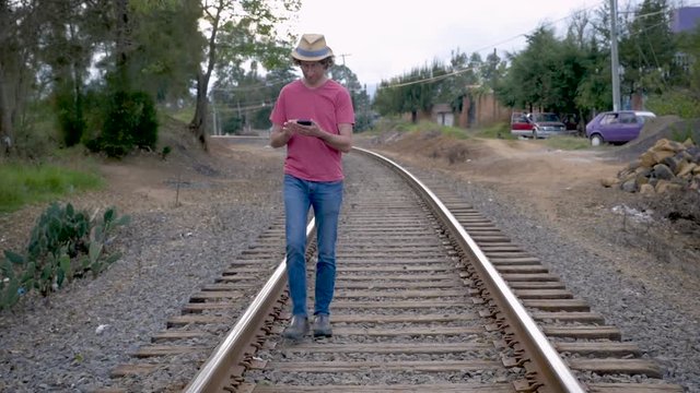 Man walking on railroad tracks while using his smart phone