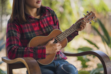 Young hipster woman sitting playing ukulele guitar at home in garden.