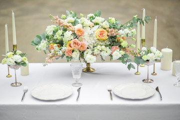 decorated wedding table for two with beautiful flower composition of flowers, glasses for wine and plates, outdoor, fine art.