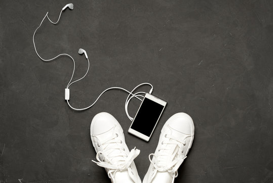 Flat Lay Of White Sneakers On Black Background With Phone And Headphones