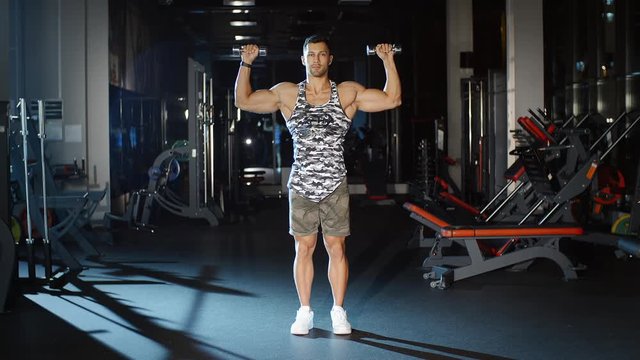 Handsome muscular man lifts hands with dumbbells workout in gym sportclub