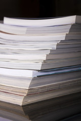 Used magazines - books stacked in a pile on a black background, a side view.