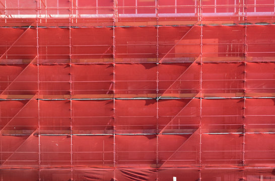 Scaffolding On A Building Construction Site Covered With Red Safety Netting