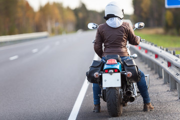 Rear view at woman on a motorcycle resting on the roadside of a country highway with empty road,...