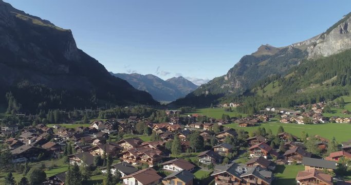 Beautiful countriside aerial shot of idyllic mountain scenery in the Alps with traditional chalets,farm in alpine meadows.Green fields,famous stunning touristic town with high cliffs in background.