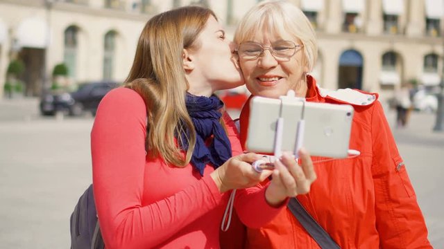 Young daughter taking selfie photo on mobile with her senior mother on vacation trip in Paris in Place Vendome. Making funny faces, kisses. Happy family enjoying vacation. Future is female