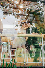 Look through the glass of the restaurant. There is an Asian bride and Asian bride talking together with laughing faces.