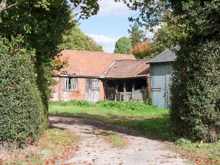 Fototapeta na wymiar old abandoned worn down farm country house outside through hedge