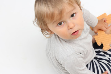 Naklejka premium baby playing with a puzzle and looking towards the camera