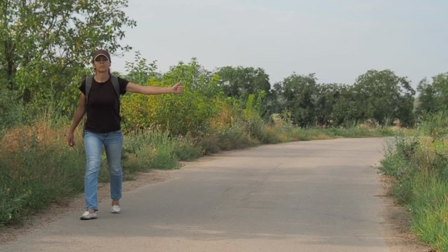 The girl is hitchhiking. A woman is walking along the road. Hitch-hiking.