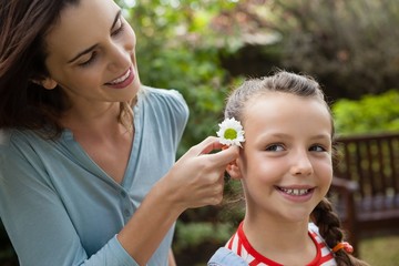 Obraz premium Smiling mother positioning white flower in hair of girl