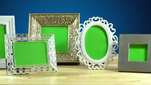 Row of various photo frames with green screen on elegant table interiors display, panning across.