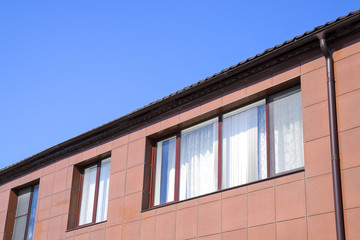 Plastic windows on the house and a spillway system on the roof. House with plastic windows and a brown roof of corrugated sheet