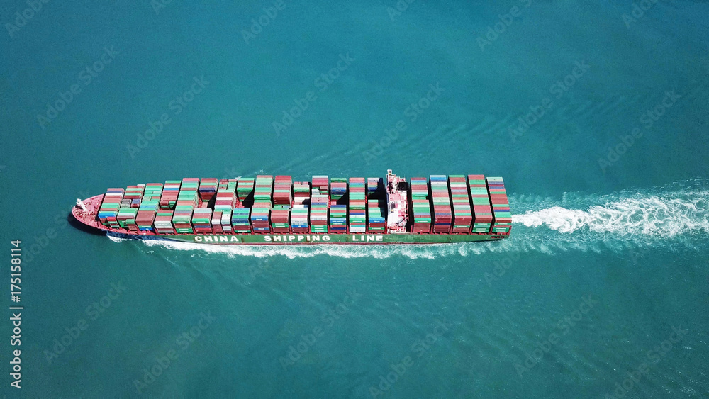 Wall mural huge large mega container ship sails on open water fully loaded with containers and cargo - aerial v