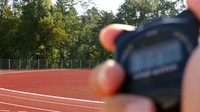 Blurred stopwatch in hand and female runner athlete on stadium