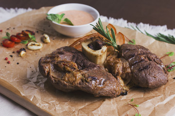 The large roasted piece of meat on the bone with sauce and spices on wooden board