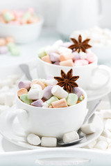 cocoa with colorful marshmallows and spices in cups, vertical