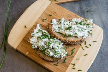 Home made bread on a wooden cutting board with curd cheese and ricotta and herbs. Decorated with green herbs 