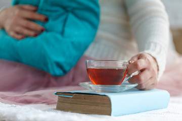 Close up of woman's hands holding a cup of tea, wearing a white sweater and enjoying the leisure time