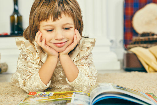 Smilling little girl lying on the floor and reading an illustrated book.