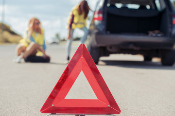 Two young girls with a broken car on the road.