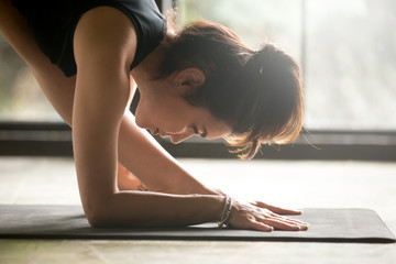 Fototapeta premium Young attractive woman practicing yoga, standing in One Sided Fold exercise, Parsvottanasana, Pyramid pose, working out, wearing black sportswear, indoor close up image, studio floor background