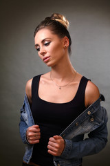 young very beautiful woman with bunched hair in a black T-shirt, having lowered a little denim jacket from her shoulders stands on a gray background, smiling, looking down to the side 