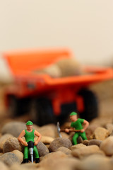 Miniature construction workers on gravel with tipper truck in the background