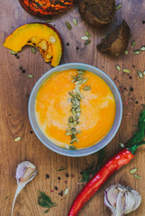 Roasted pumpkin soup with cream and pumpkin seeds on wooden background. top view