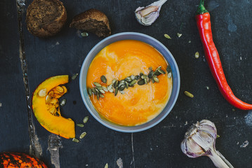 Roasted pumpkin soup with cream and pumpkin seeds on dark wooden background. top view