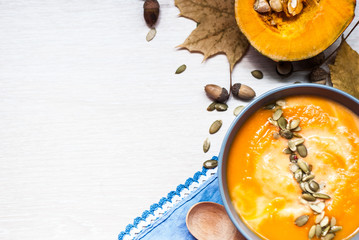 Pumpkin soup with cream and pumpkin seeds on a white wooden table. top view. copy space