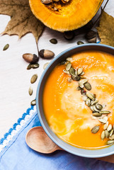 Pumpkin soup with cream and pumpkin seeds on a white wooden table. top view. copy space