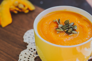 Roasted pumpkin soup with cream and pumpkin seeds on wooden background.