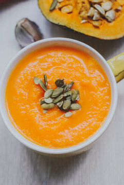 Roasted pumpkin soup with cream and pumpkin seeds on wooden background.
