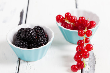 röda vinbär och björnbär i turkosa porslins skålar mot vit trä bakgrund