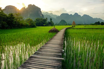 Fotobehang Zonsondergang over groene rijstvelden en bergen in Vang Vieng, Laos © Jeff