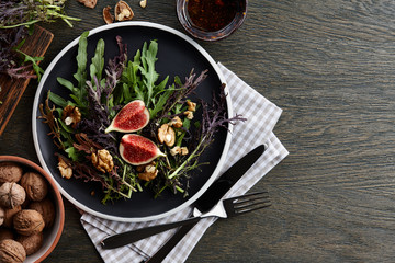 Seasonal salad with figs, walnuts and fresh greens on wooden background, top view