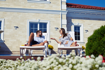 Happy couple talking while relaxing on lounge chairs in front of house