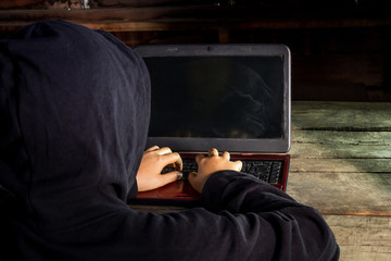 Hacker in front of his computer in the room with light and dark wooden floor.