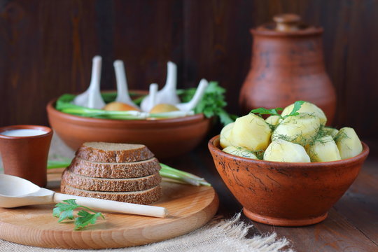 Fresh boiled potatoes. Boiled potatoes in a clay bowl with greens and vegetables on a dark wood background.