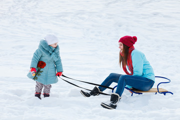 Little girl is driving mom on sledging in the snow in winter