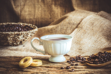 The vintage style of a white coffee cup and coffee beans on wooden sheet.Old sackcloth background.