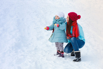 A young mother with a little daughter walks in the winter and looks at something interesting