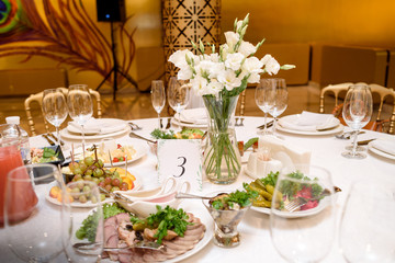 Beautiful fresh flowers on table in wedding day, free space. Bouquet of white eustoma in glass vase on dinner table in restaurant with gold interior