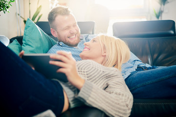Couple using tablet while laying on sofa in living room